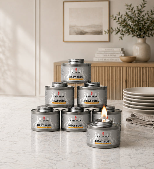Caterpax heat fuel cans on a table with a lit candle, in a home setting.