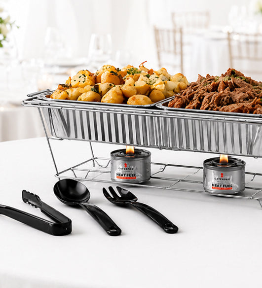 Food display with pulled pork, roast potatos, and other items on a white surface with black utensils.